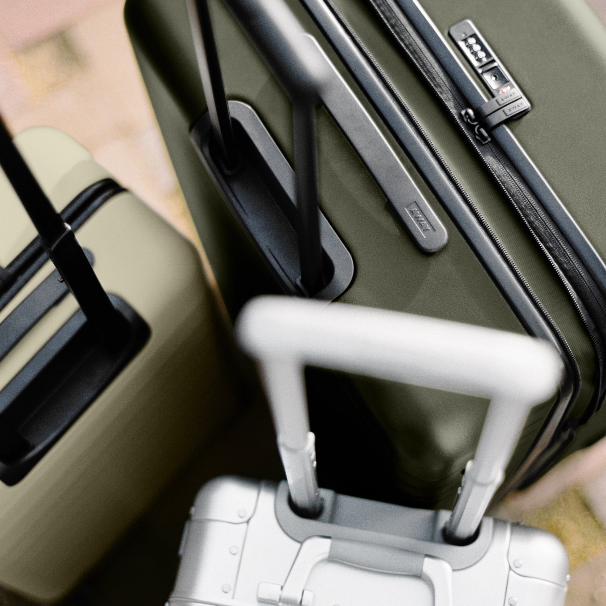Top view photo of The Medium Flex in Olive Green, The Bigger Carry-On in Salt White, and The Carry-On: Aluminum Edition showing luggage handles and lock