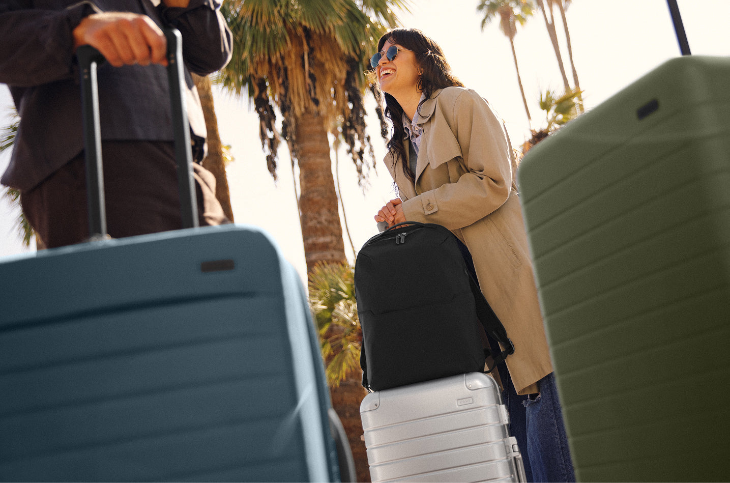 A person traveling with an Everywhere Zip Backpack and Aluminum suitcase, Softside luggage, and hardside suitcase