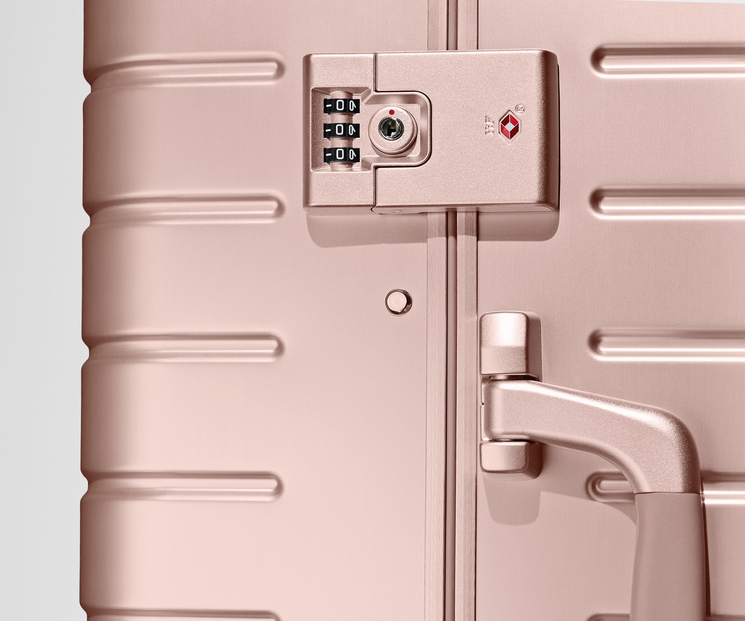 Close up view of the TSA lock on the side of a Rose Gold Aluminum suitcase