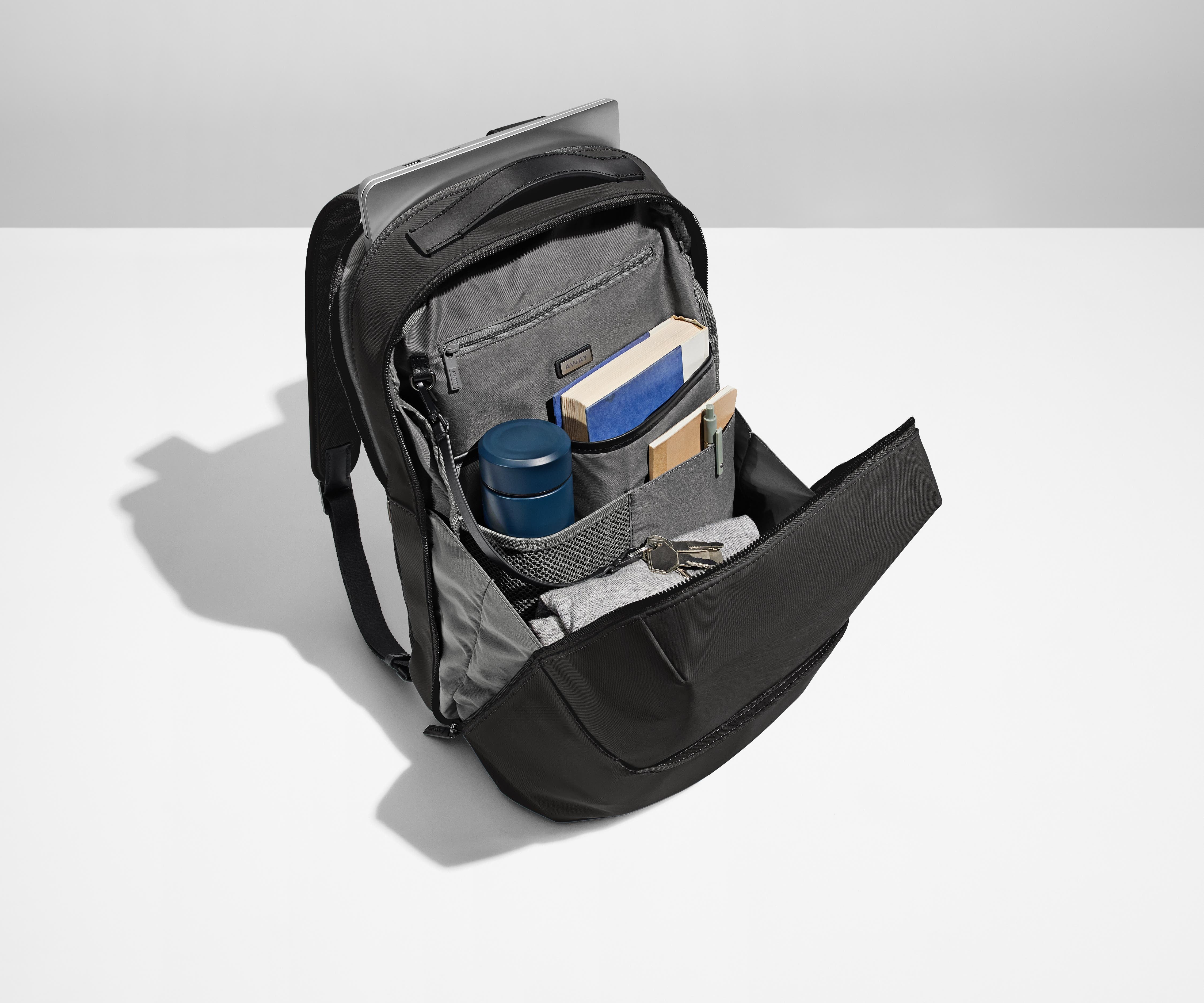 Main compartment of the Black Everywhere Zip Backpack packed with a water bottle, books, light layer of clothing, and key attached to a key leash. A laptop is packed in the exterior laptop pocket
