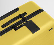 The Large suitcase in Sunshine Yellow shown shown from above highlighting TSA-approved combination lock and recycled leather luggage tag