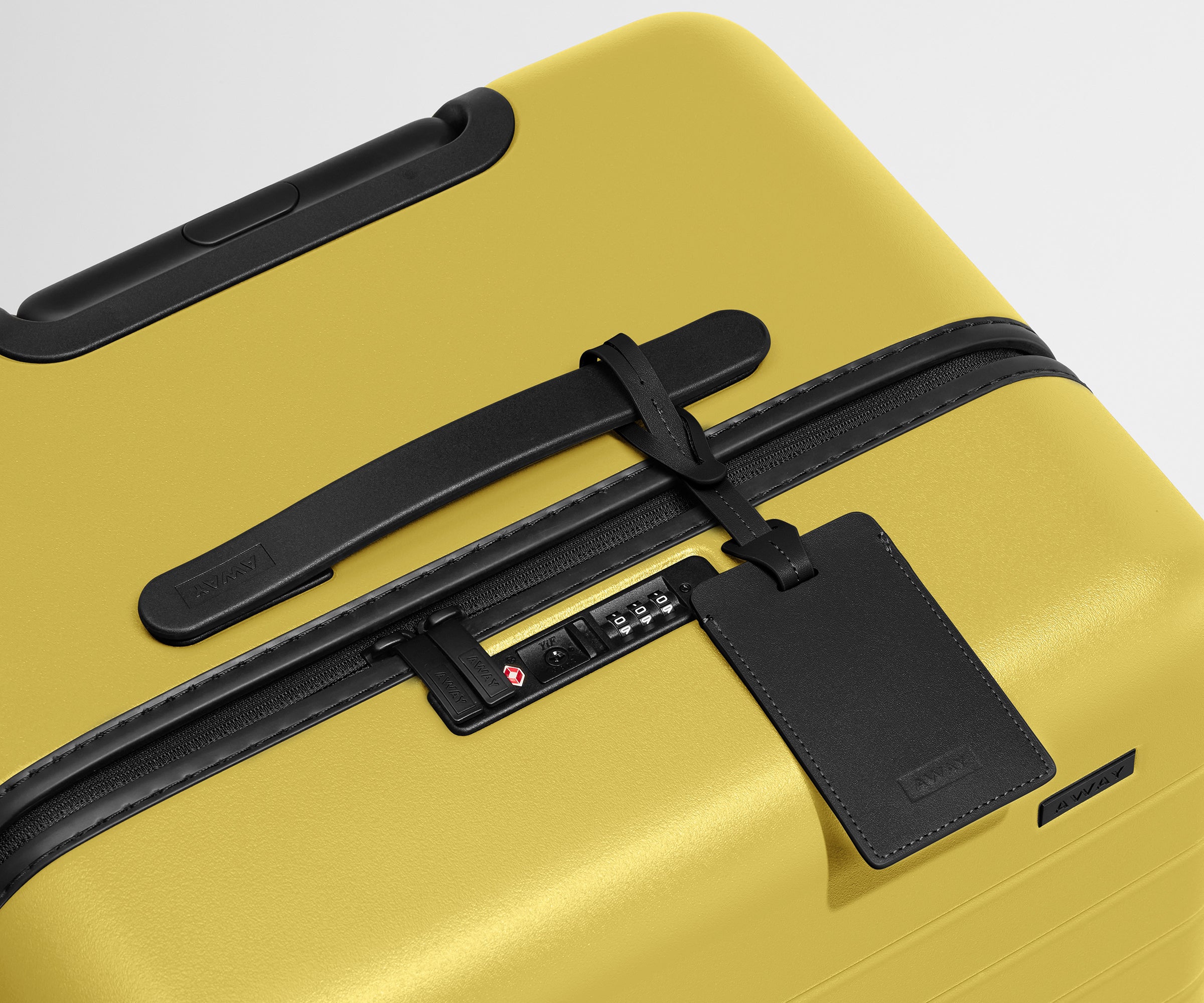The Trunk suitcase in Sunshine Yellow shown shown from above highlighting TSA-approved combination lock and recycled leather luggage tag