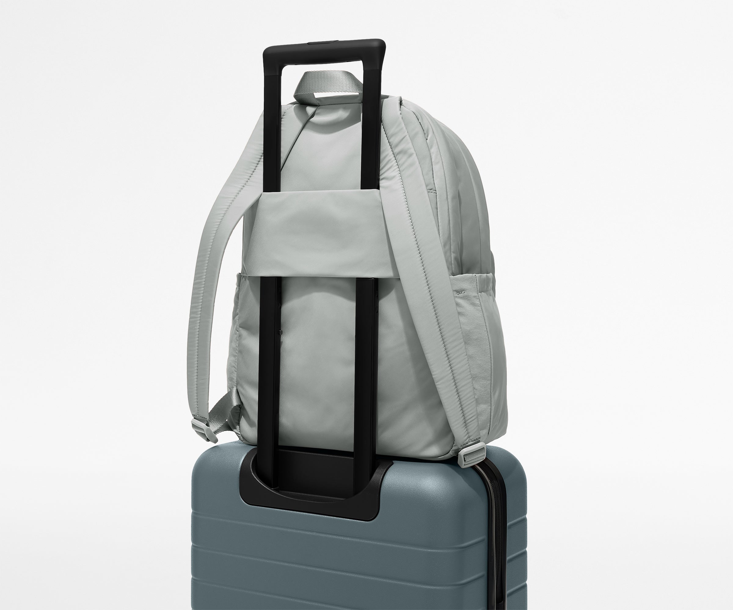 Gray backpack with black handle attached to a suitcase on a light gray background