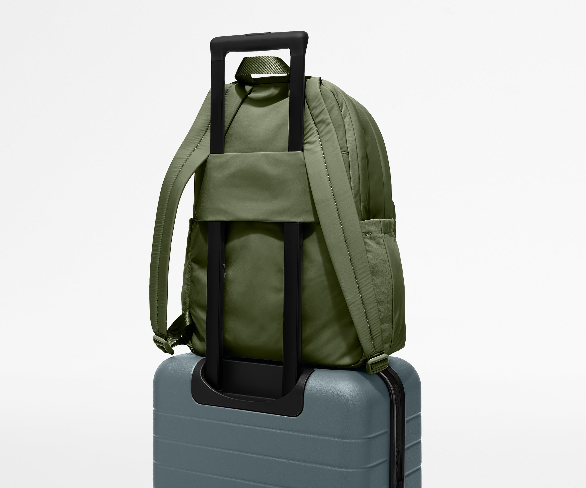Green backpack with rolling handle on a gray suitcase against a light gray background
