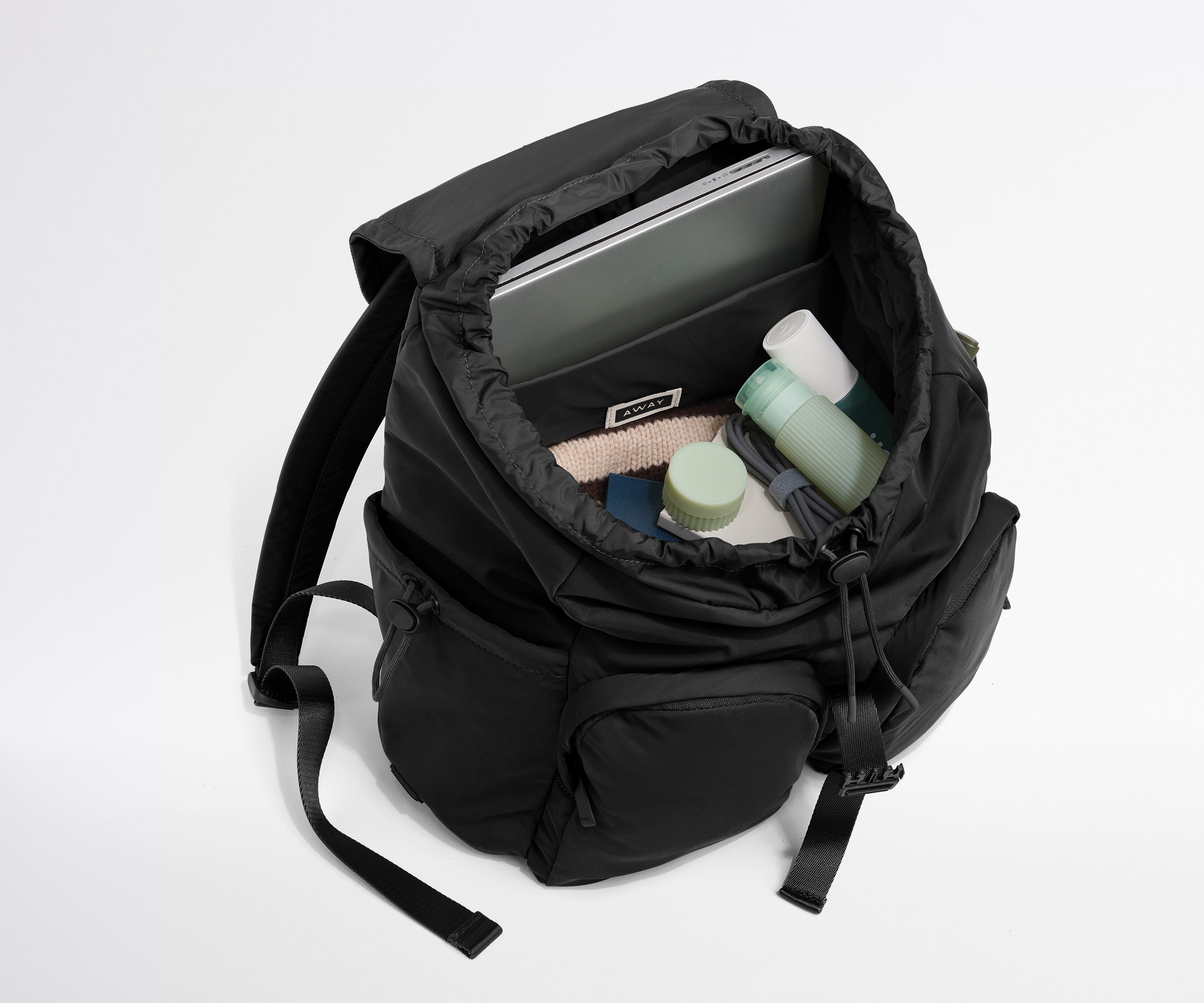 Black backpack with compartments containing a laptop, towel, and bottles on a white background