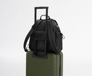 Black backpack with a shoulder strap on top of a green suitcase against a light gray background