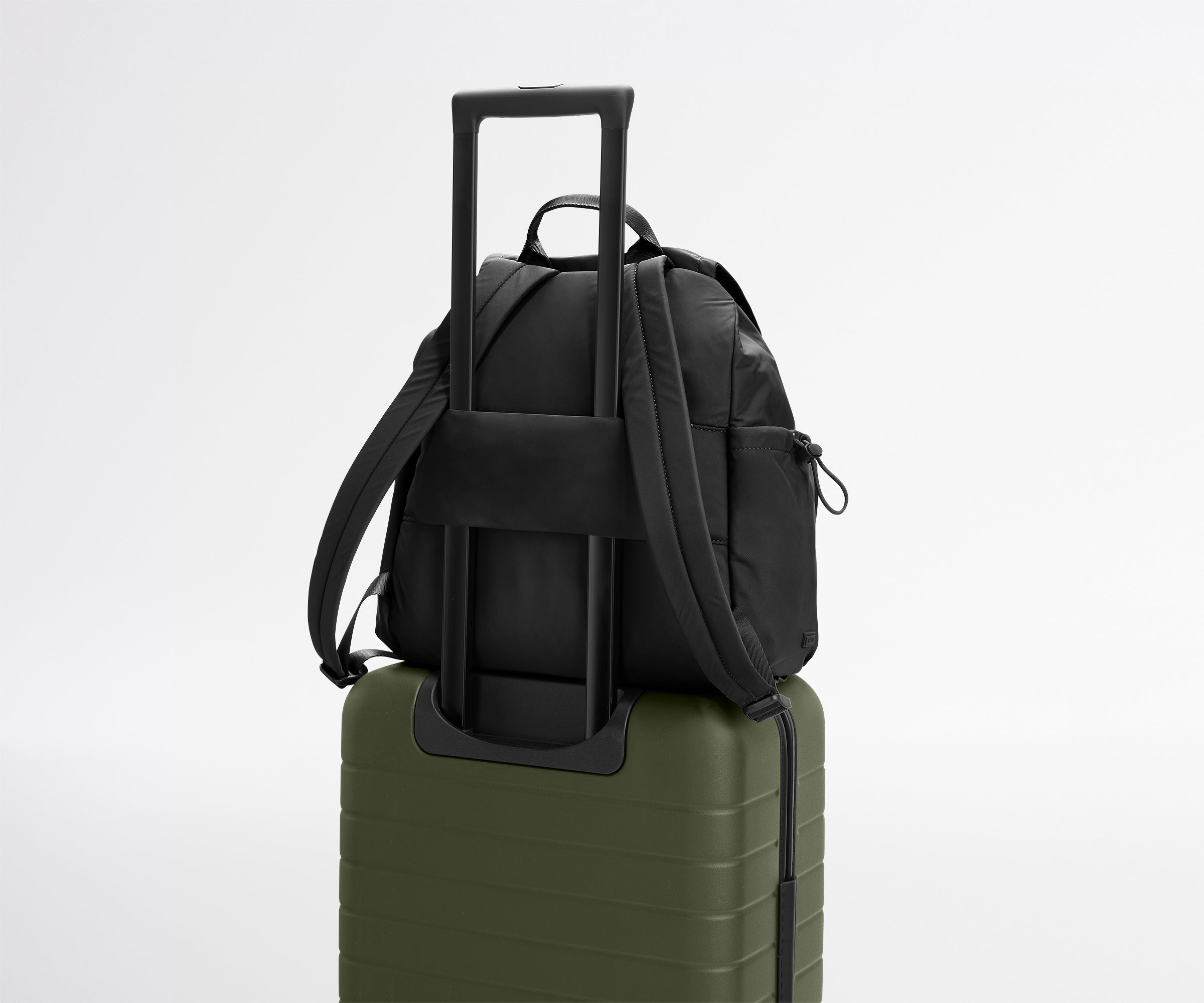 Black backpack with a shoulder strap on top of a green suitcase against a light gray background