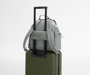Gray backpack with a shoulder strap on top of a green suitcase against a light gray background
