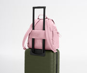 Pink backpack on top of a green suitcase with a white background