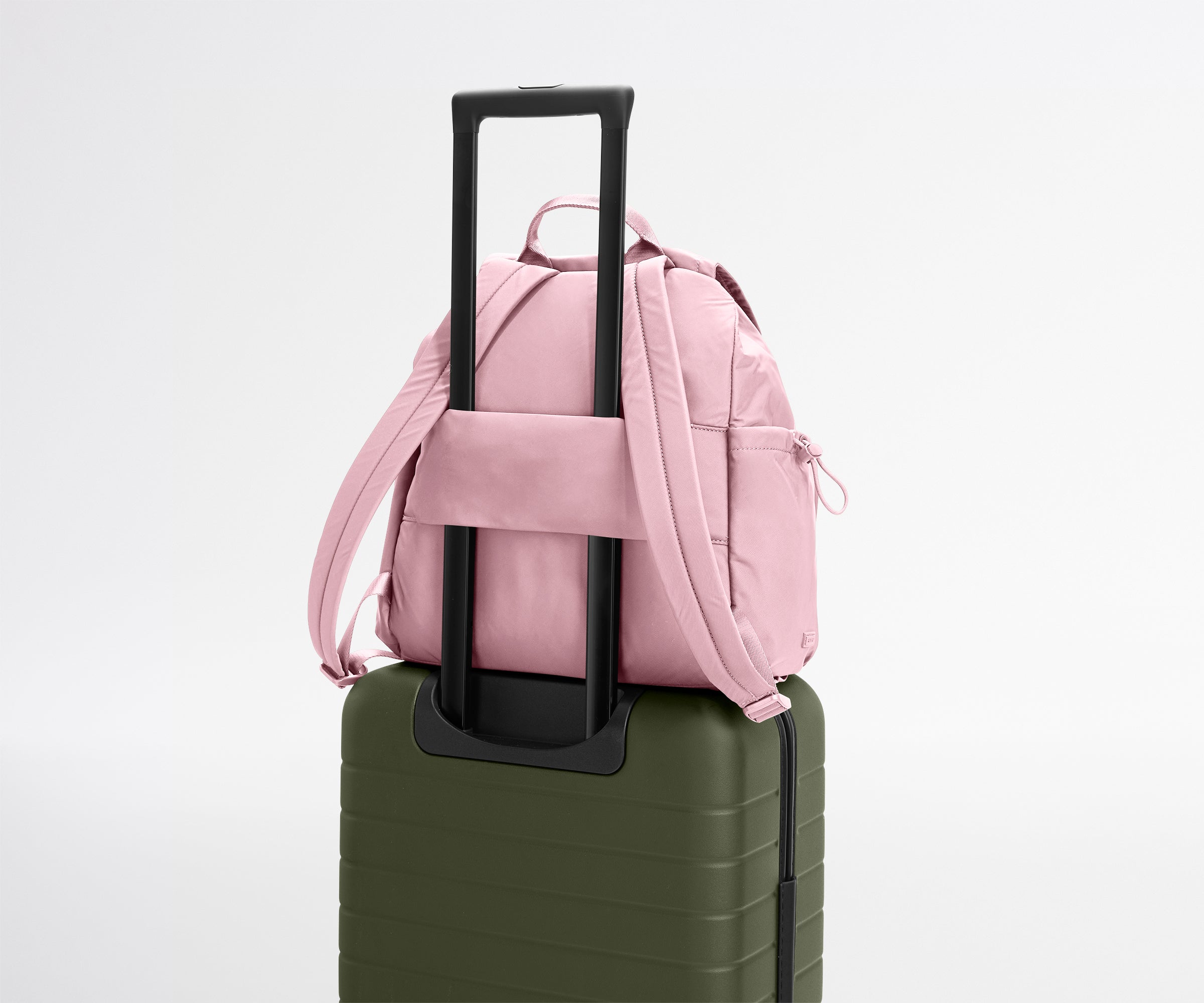 Pink backpack on top of a green suitcase with a white background
