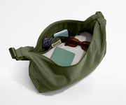 Green bag with items like sunglasses and a phone on a white background