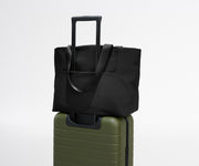 Black tote bag on top of a green suitcase against a white background