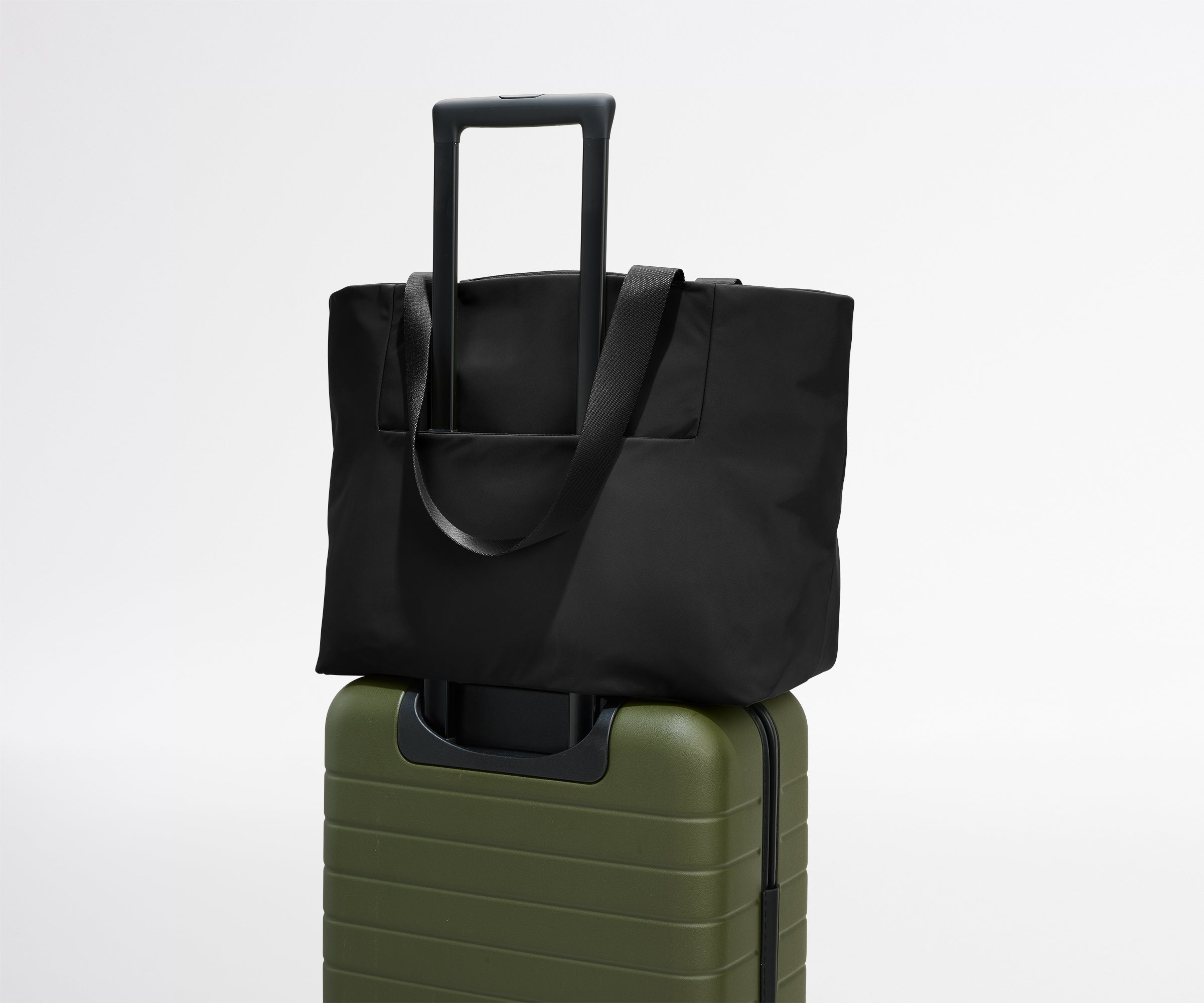 Black tote bag on top of a green suitcase against a white background