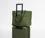 Green tote bag on top of a green suitcase against a white background