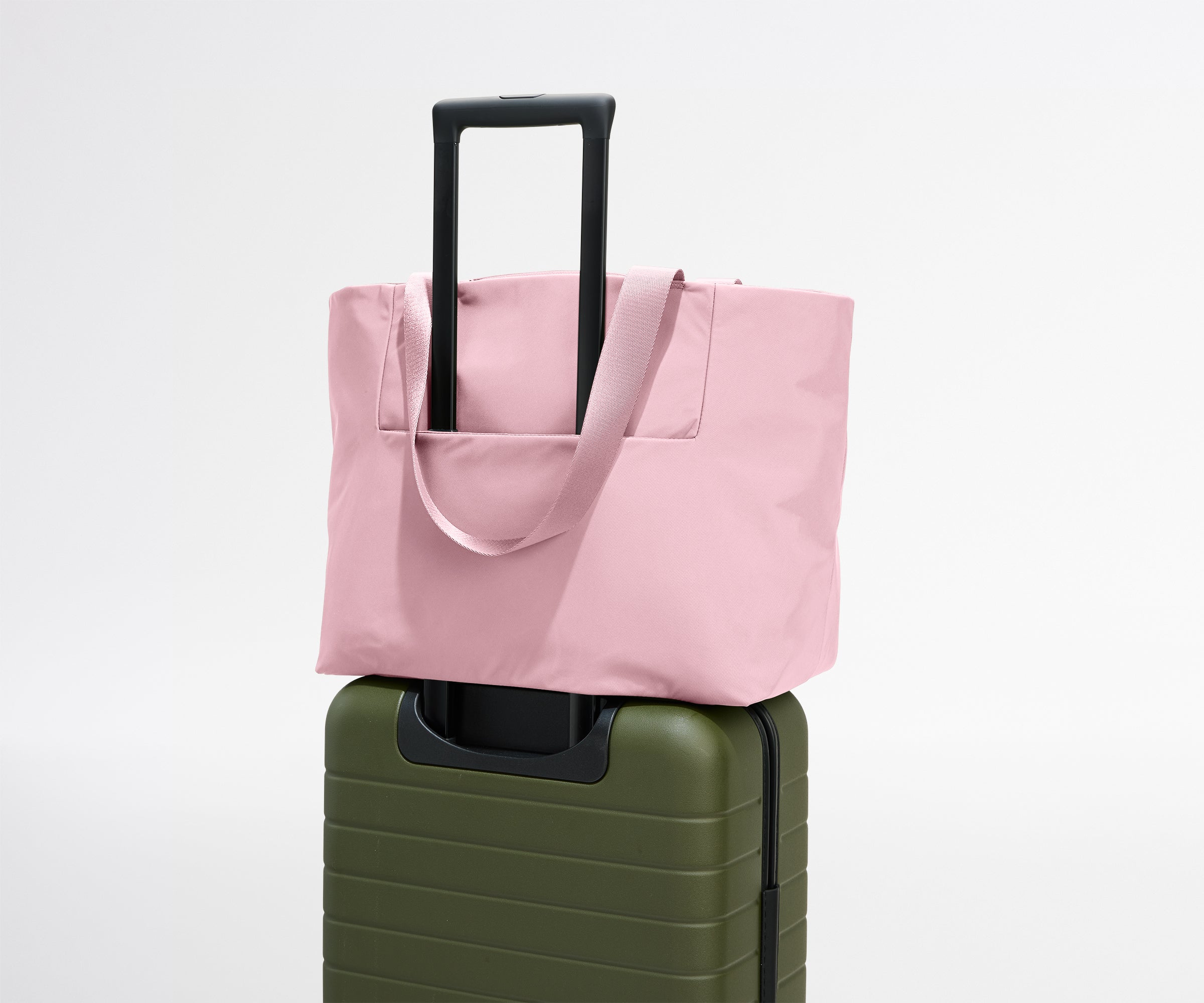 Pink tote bag on top of a green suitcase against a white background