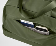 Green duffel bag with a pocket containing a passport and phone on a light gray background