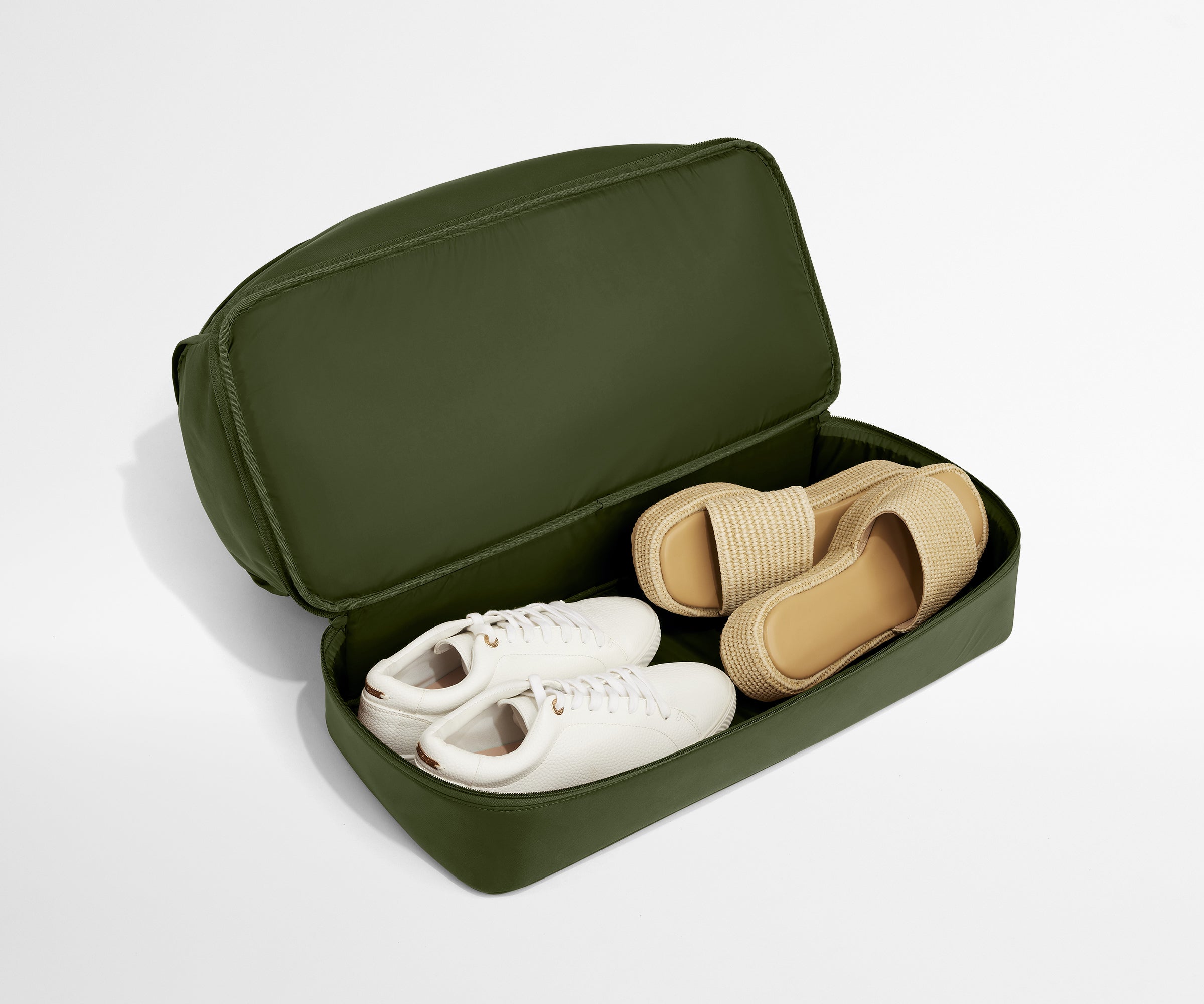 Green travel shoe case with white and beige shoes on a light gray background