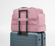 Pink backpack on top of a blue suitcase against a light gray background