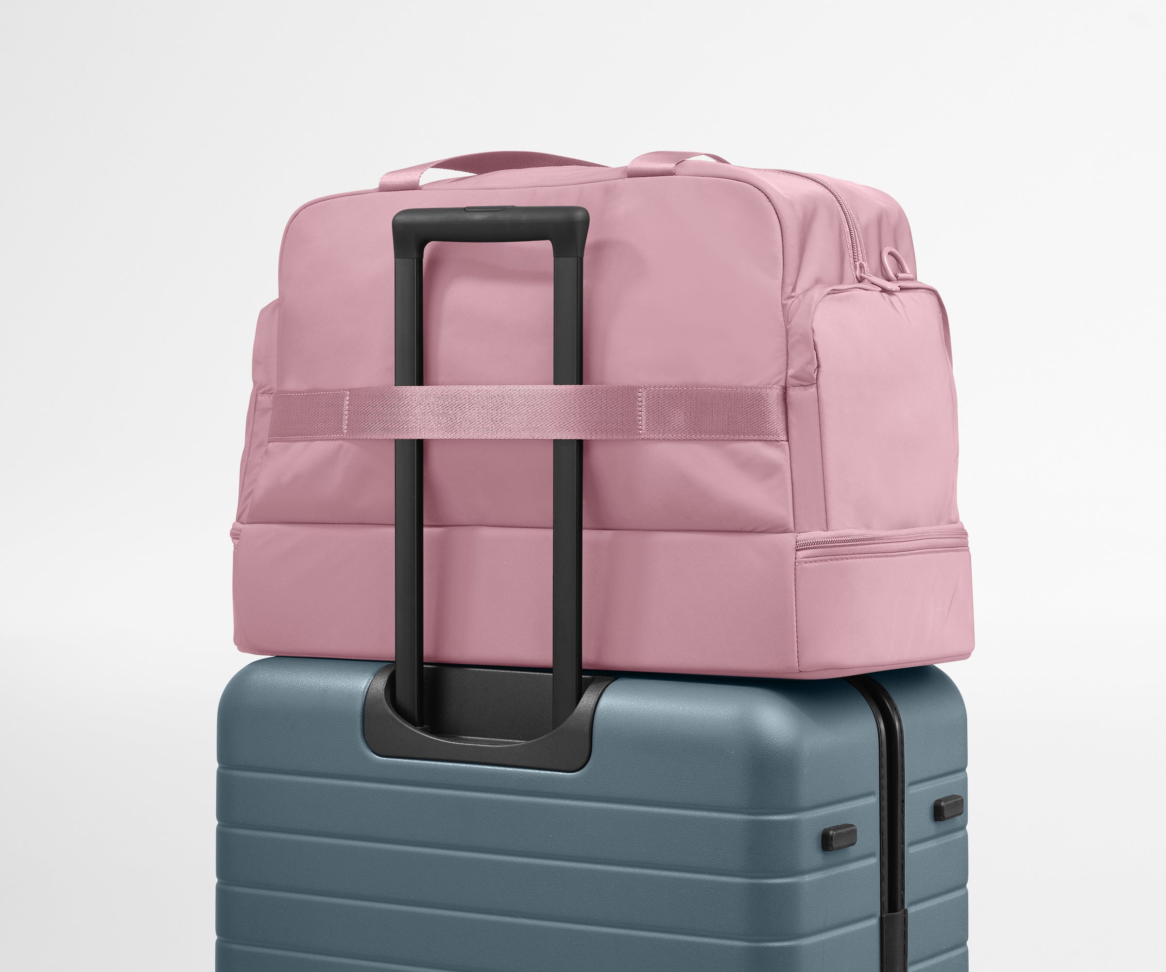 Pink backpack on top of a blue suitcase against a light gray background
