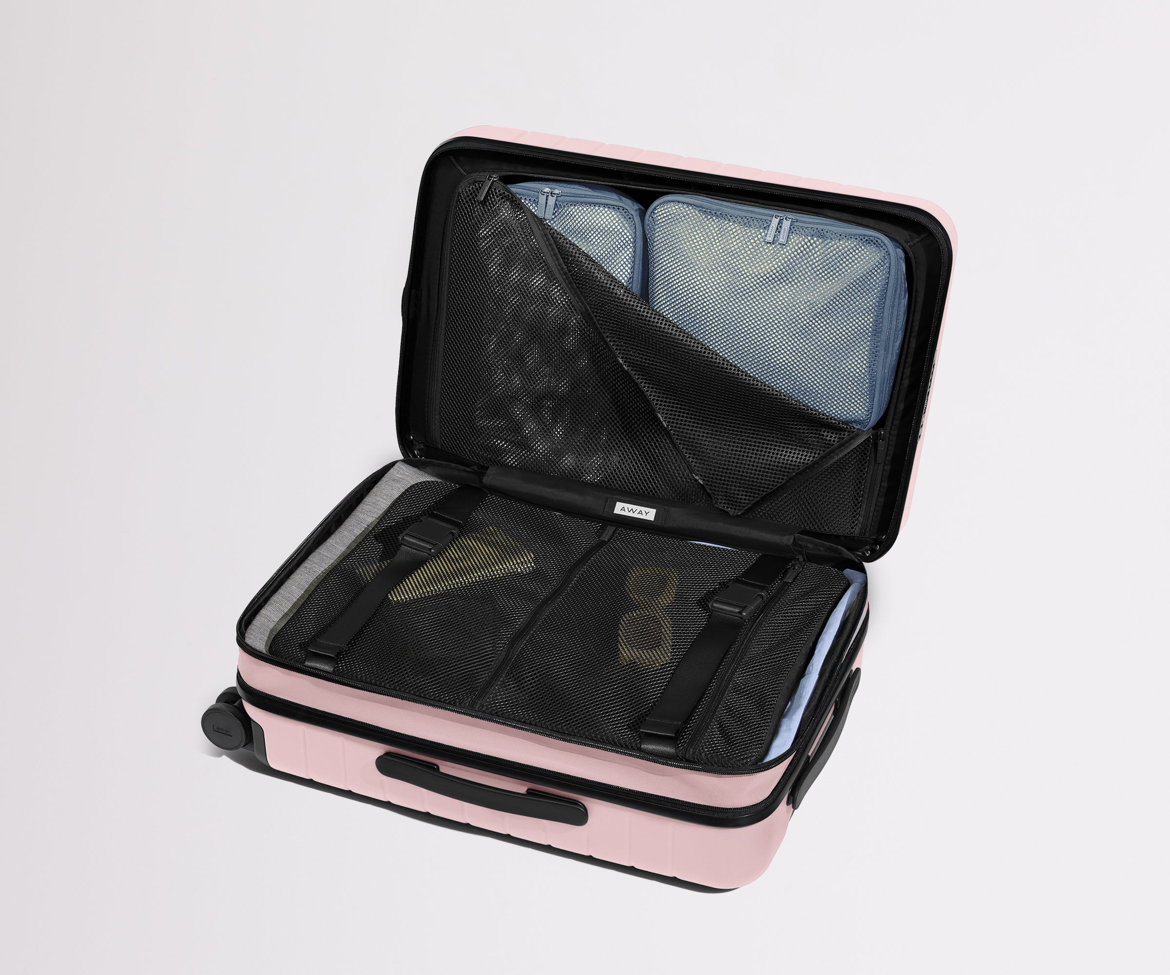 The Bigger Carry-On Flex suitcase in Blush Pink shown open on its side and packed with Away's packing organizers to show capacity and the interior compression system, designed to help you pack more in