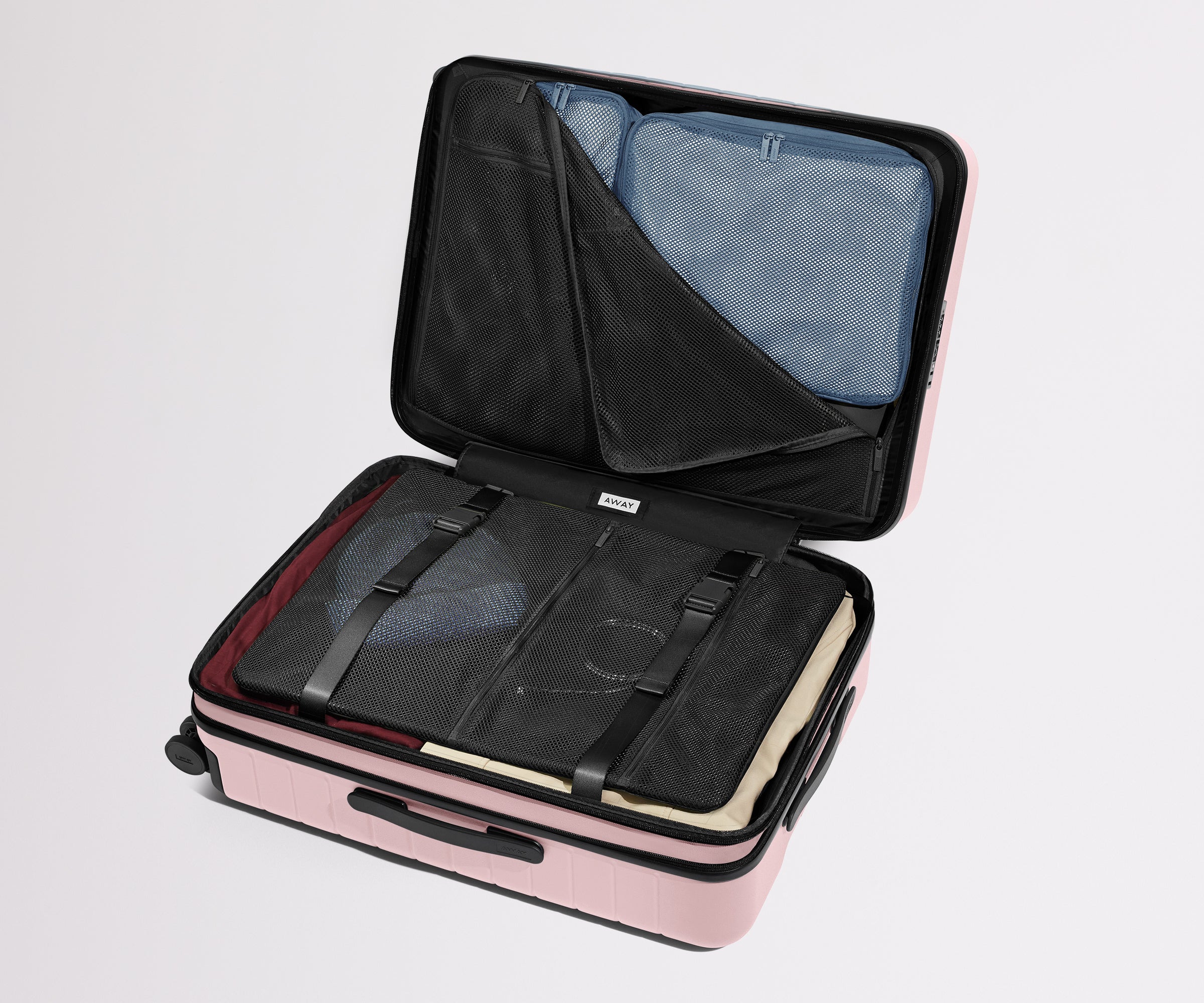 The Medium Flex suitcase in Blush Pink shown open on its side and packed with Away's packing organizers to show capacity and the interior compression system, designed to help you pack more in