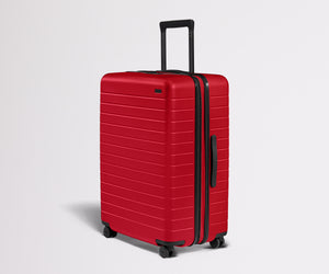 Red suitcase with black handle and wheels on a light gray background