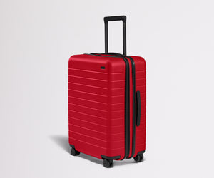 Red suitcase with black handle and wheels on a light gray background