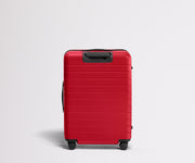 Red suitcase with black handle and wheels on a light gray background