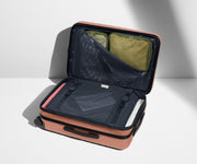 The Carry-On Flex suitcase in Clay Pink shown open on its side and packed with Away's packing organizers to show capacity and the interior compression system, designed to help you pack more in