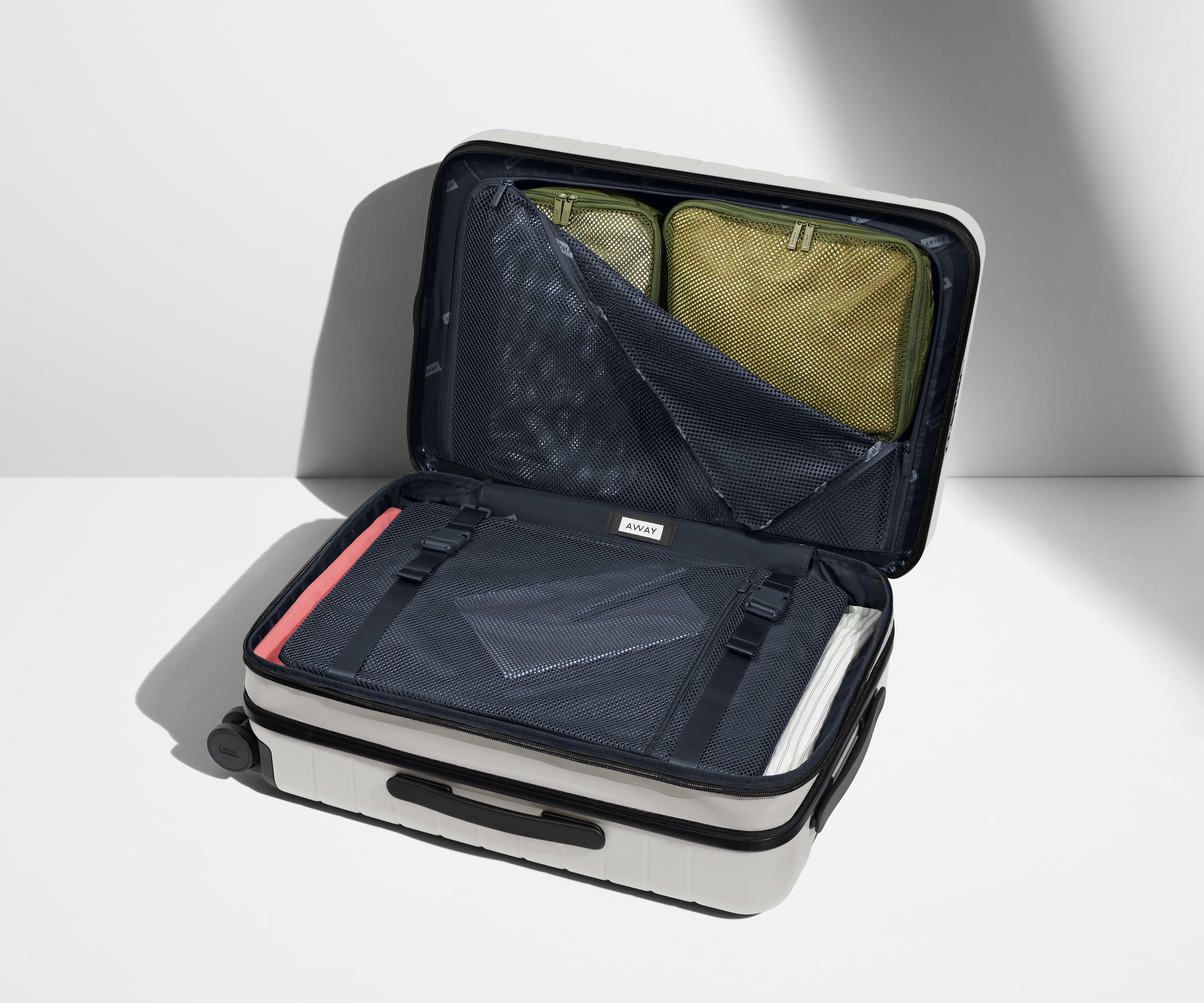 The Carry-On Flex suitcase in Cloud Gray shown open on its side and packed with Away's packing organizers to show capacity and the interior compression system, designed to help you pack more in