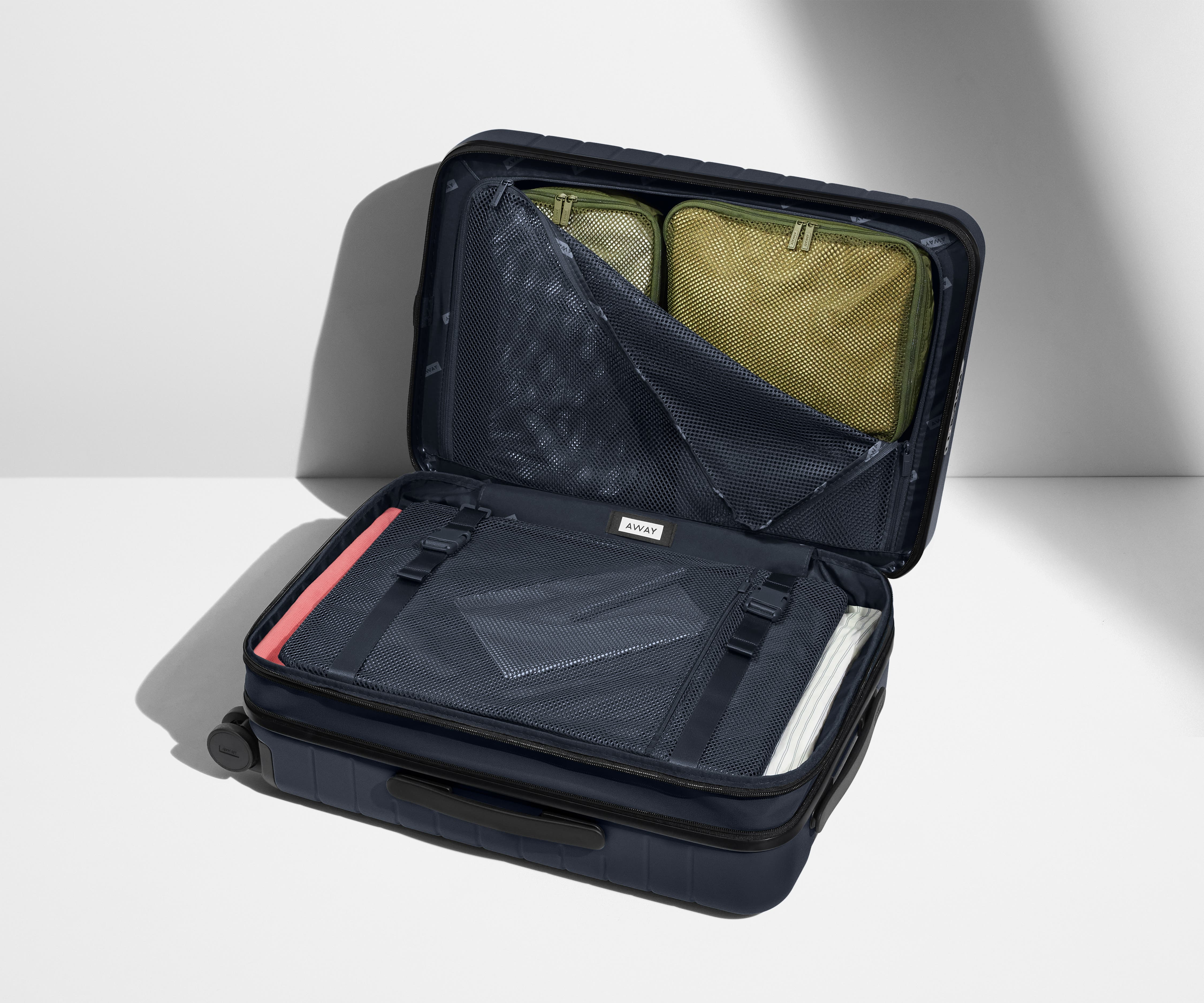 The Carry-On Flex suitcase in Navy Blue shown open on its side and packed with Away's packing organizers to show capacity and the interior compression system, designed to help you pack more in