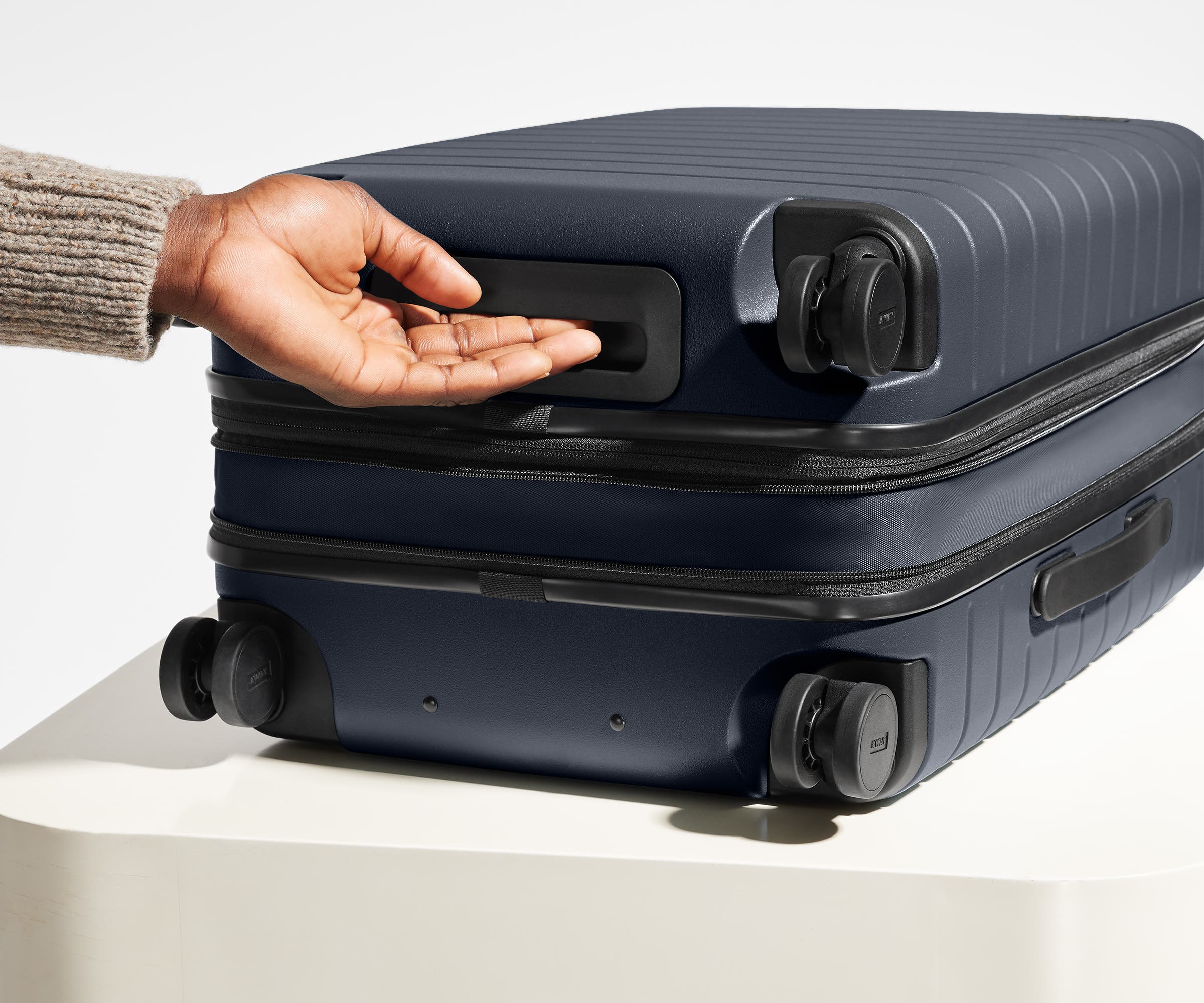 The Bigger Carry-On Flex suitcase in Navy Blue shown from below highlighting the underside grab handle