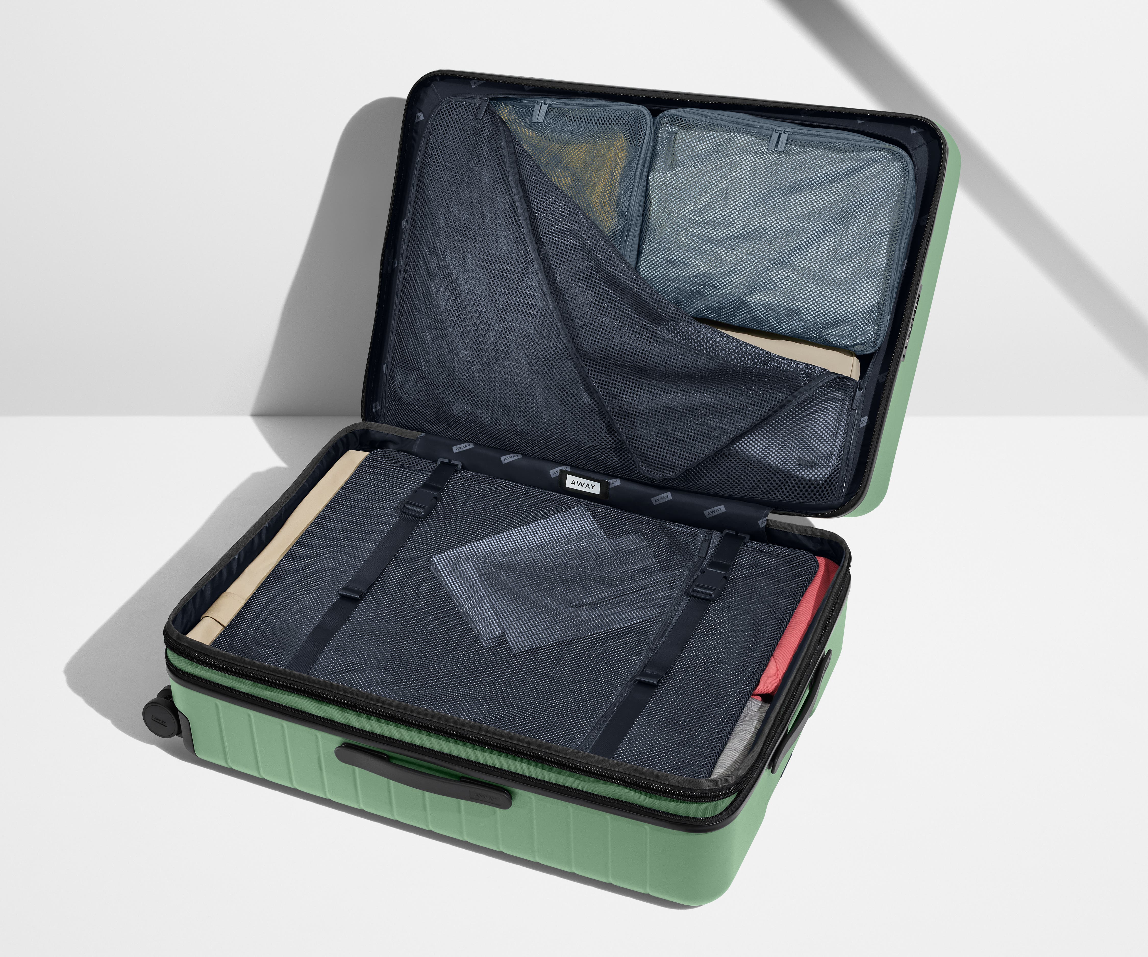 The Large Flex suitcase in Sea Green shown open on its side and packed with Away's packing organizers to show capacity and the interior compression system, designed to help you pack more in