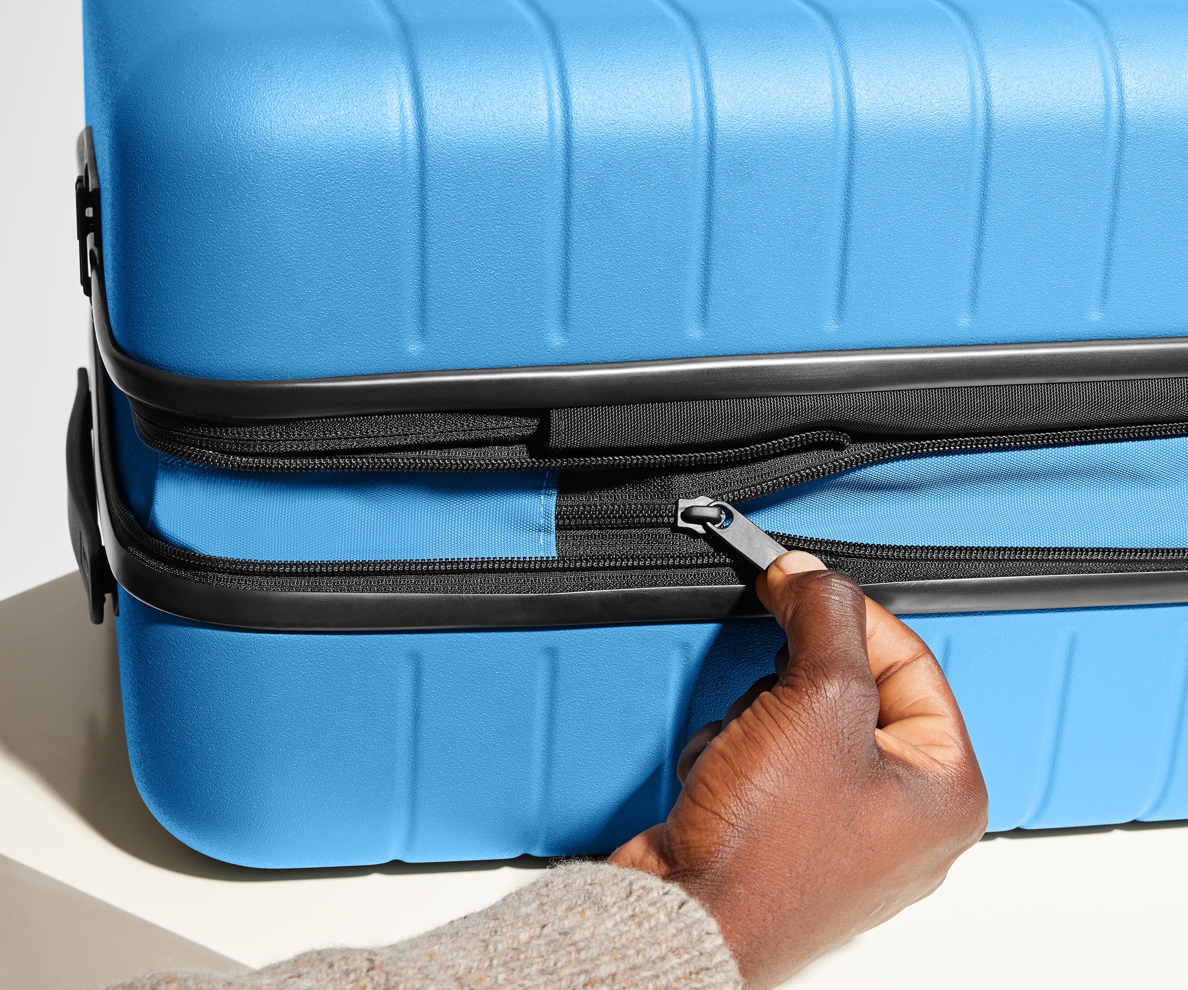 A model unzipping the wraparound zipper to expand the Flex suitcase in Splash Blue and create more packing space