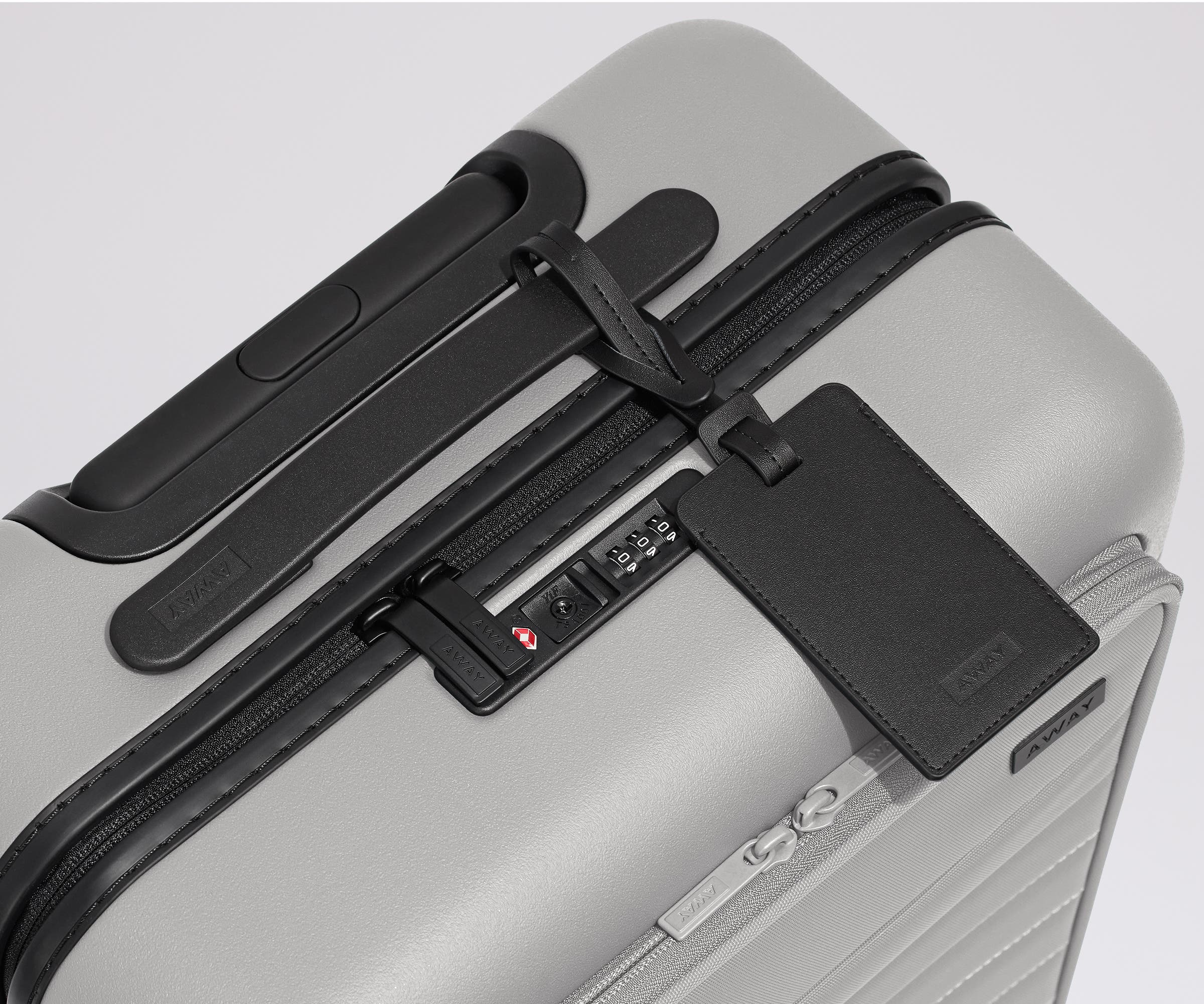 The Front Pocket Carry-On suitcase in Cloud Gray shown shown from above highlighting TSA-approved combination lock and black leather luggage tag