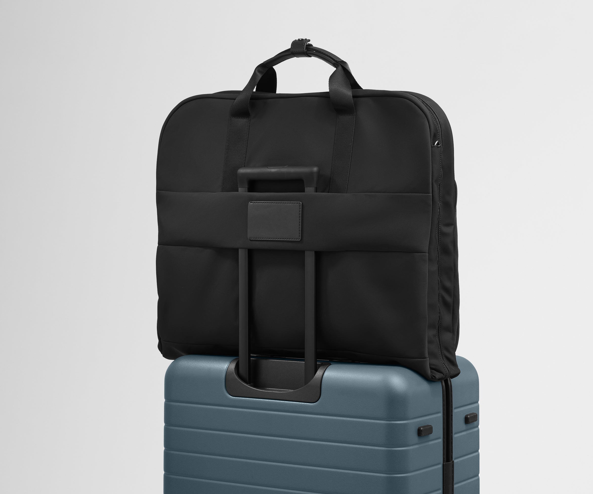 The trolley sleeve on the back of the Garment Bag in Jet Black slides over the trolley handle of an Away Medium suitcase in Coast Blue to make travel seamless