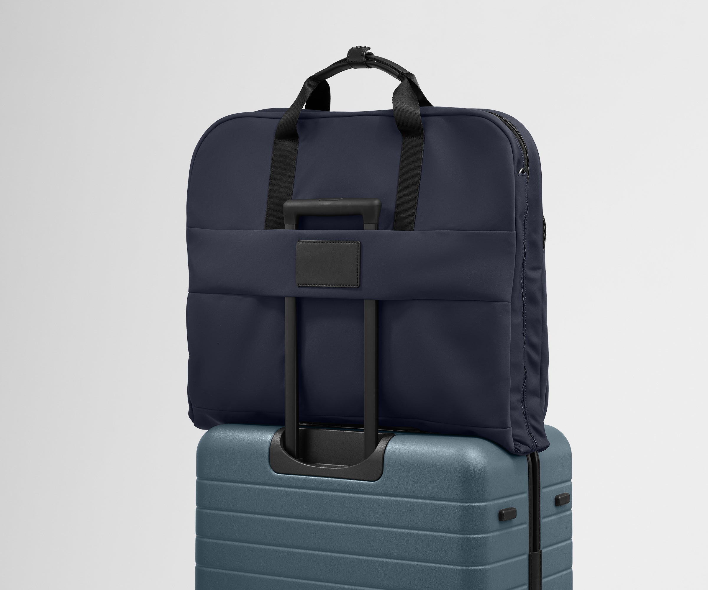 The trolley sleeve on the back of the Garment Bag in Navy Blue slides over the trolley handle of an Away Medium suitcase in Coast Blue to make travel seamless