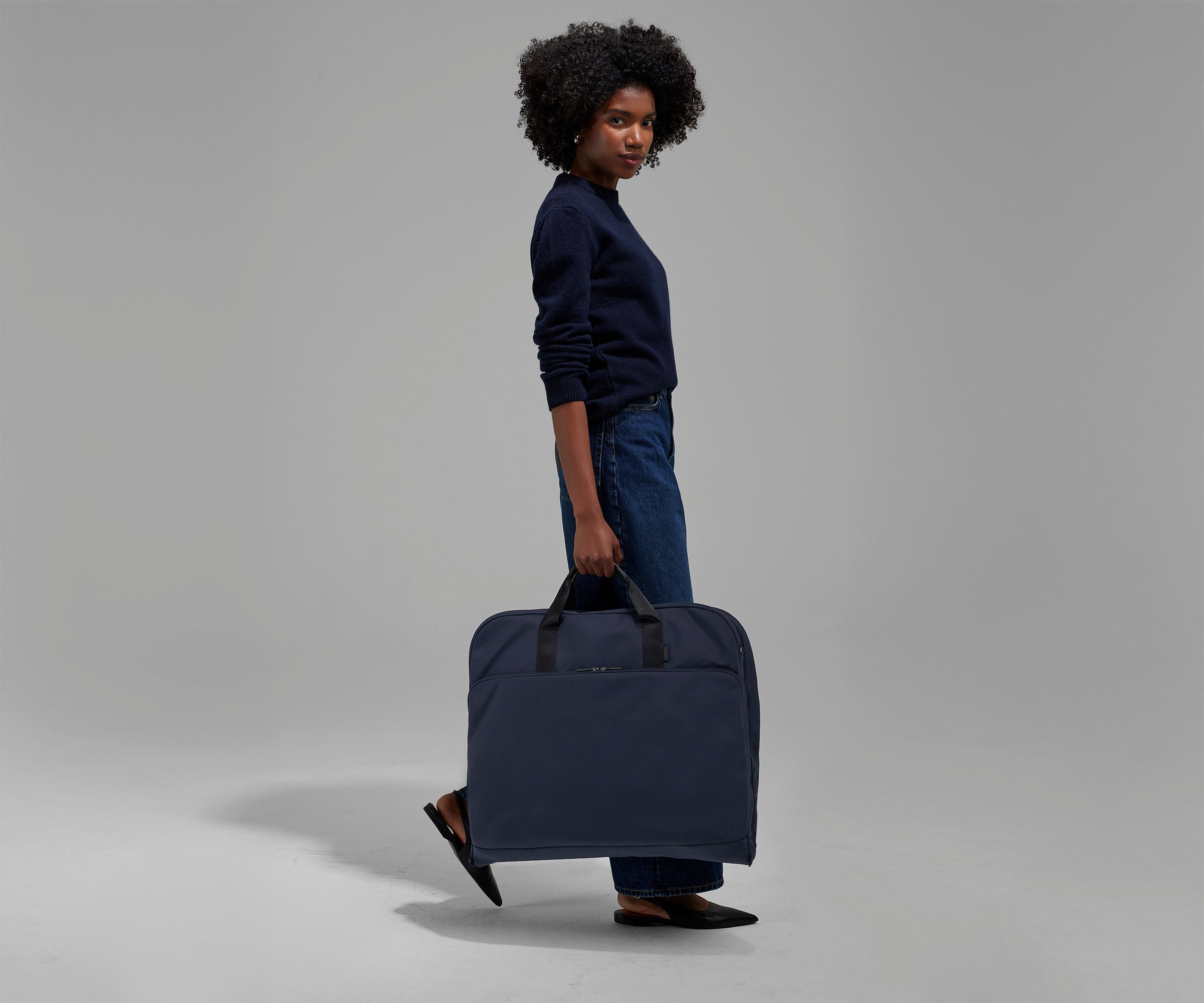A female model carrying the Garment Bag in Navy Blue using the top grab handles