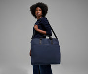 A female model carrying the Garment Bag in Navy Blue over her shoulder using the adjustable, removable shoulder strap