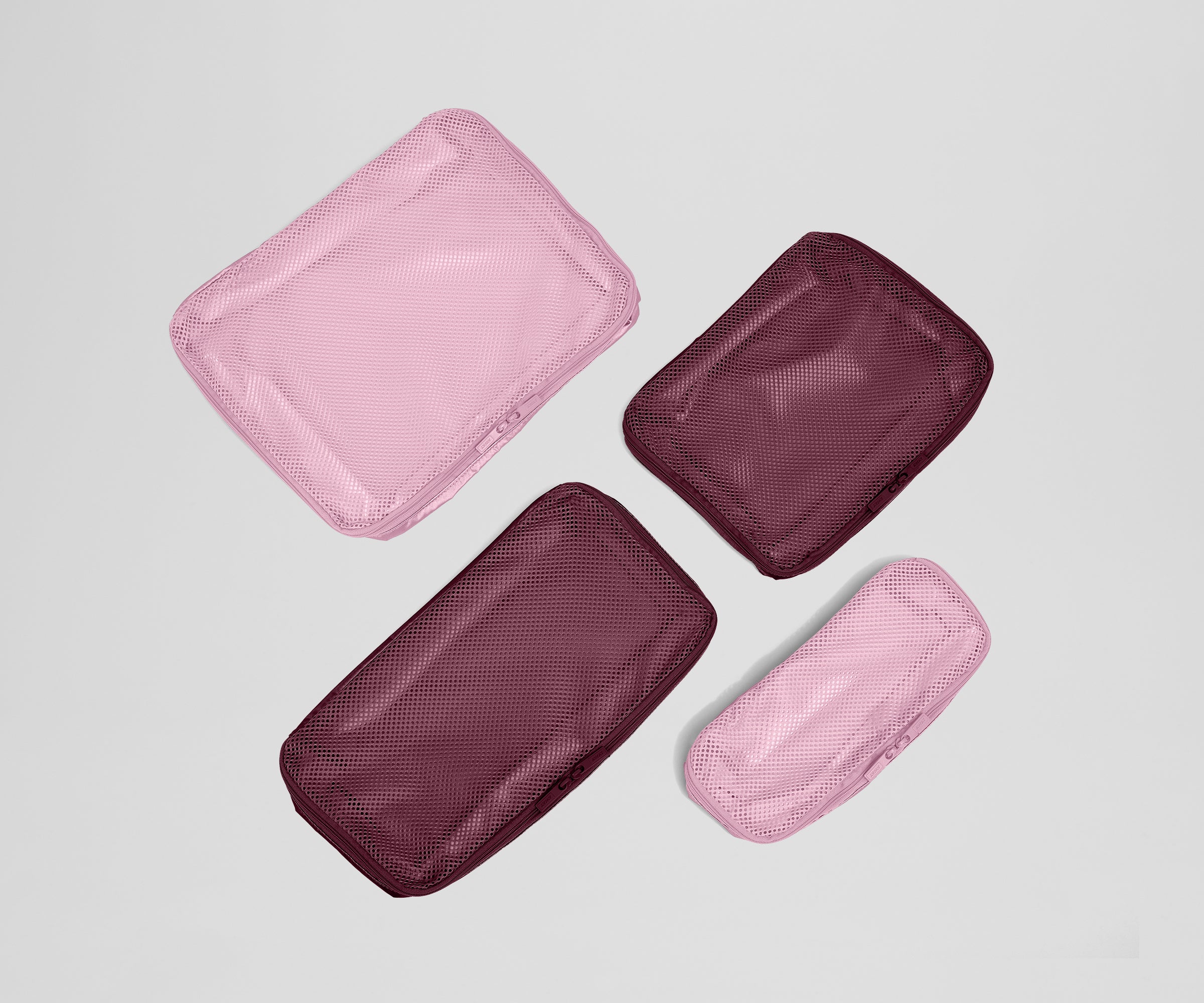 Four mesh packing cubes in pink and maroon on a light gray background