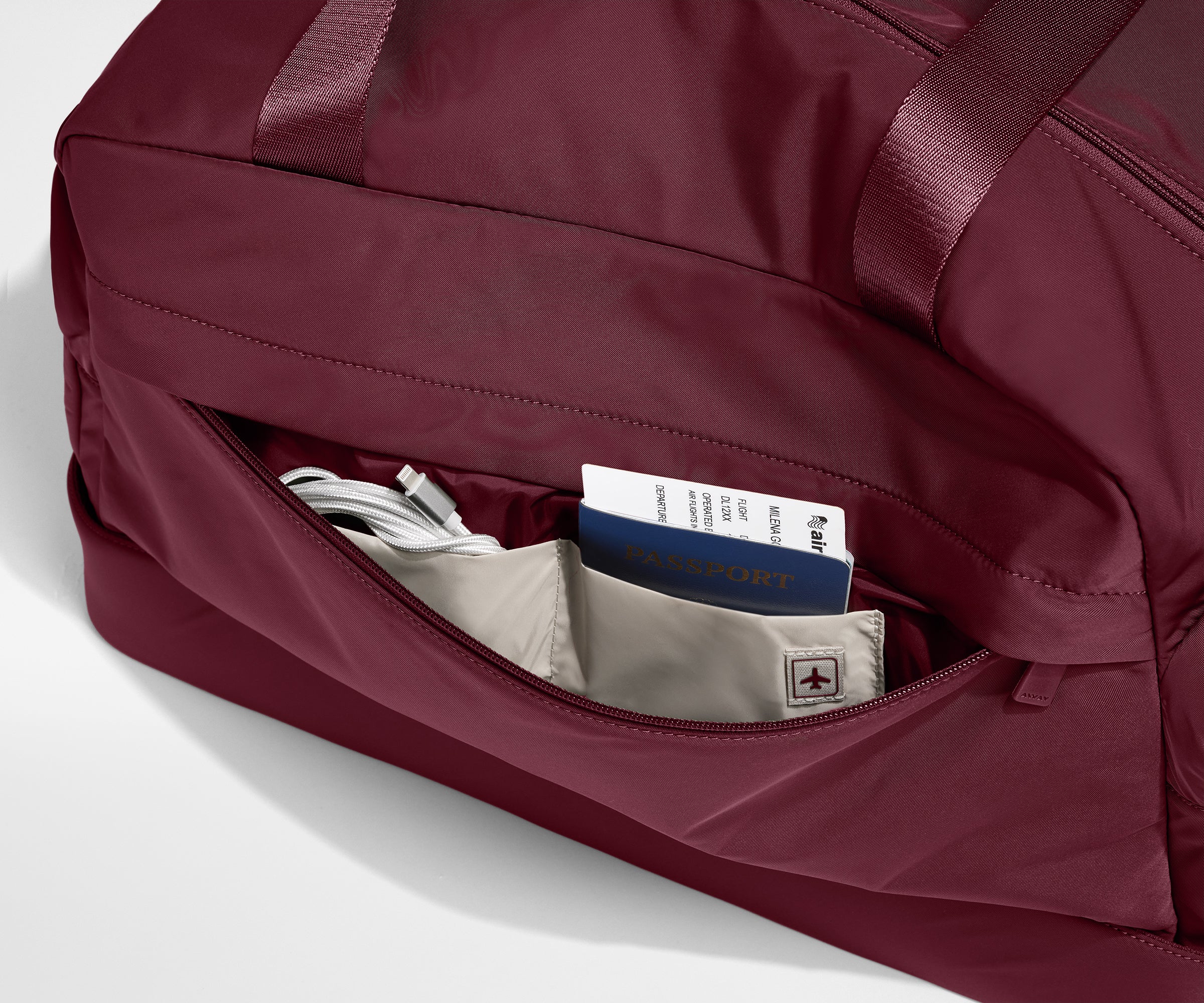 Maroon tote with a pocket open, revealing travel documents and cables.