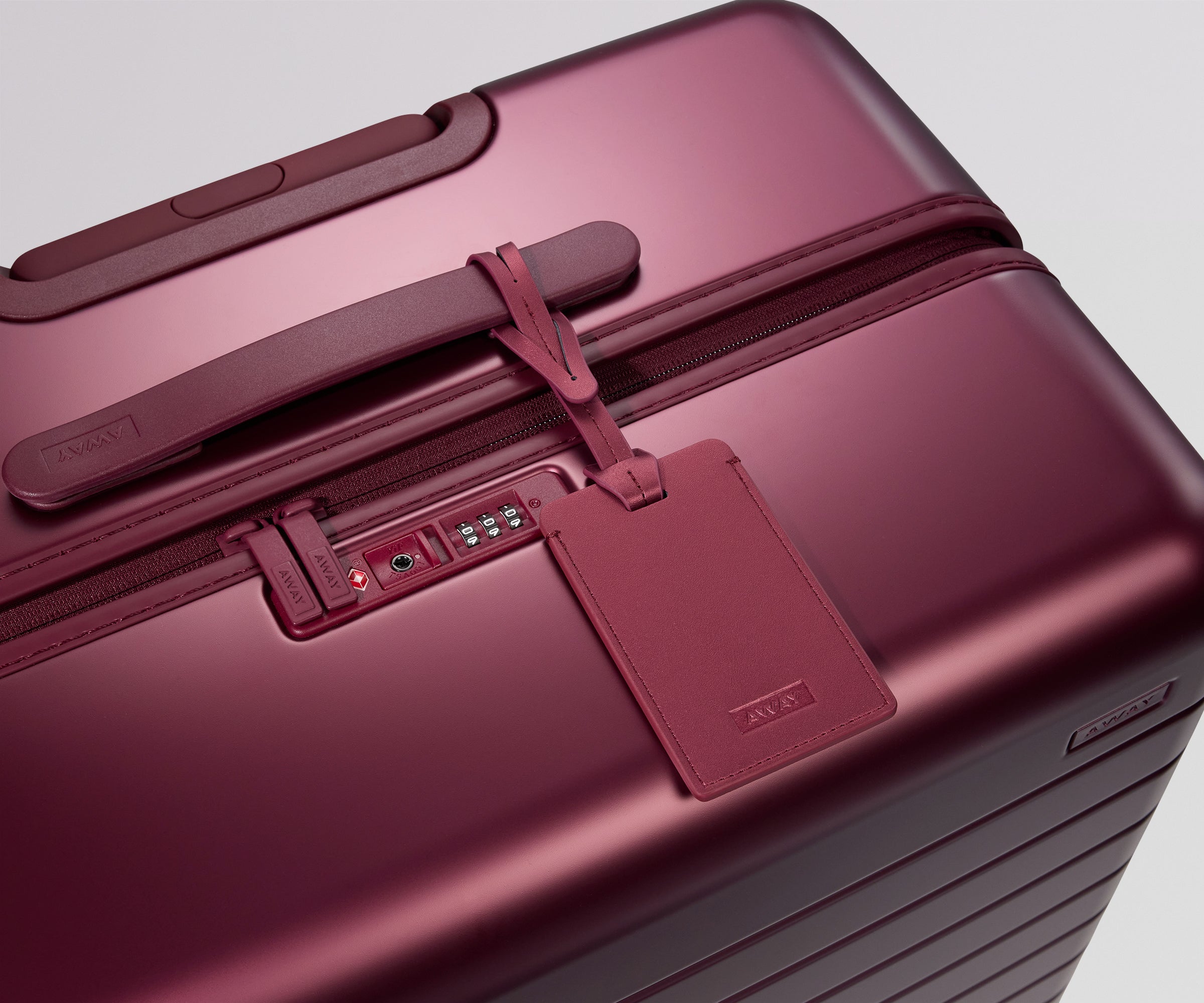 Maroon suitcase with a matching luggage tag on a light gray background
