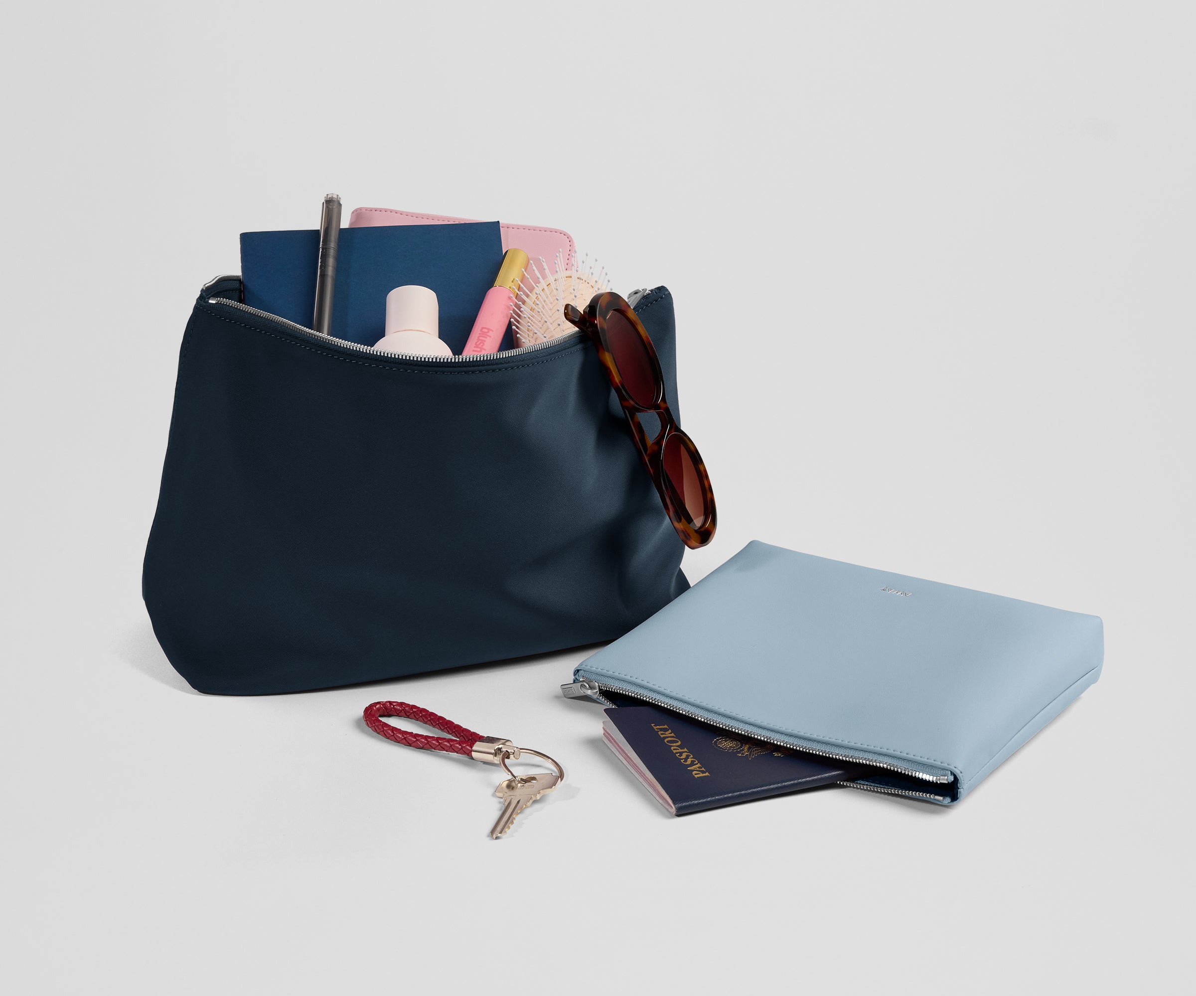 Navy pouch with items like sunglasses, passport, and keychain on a light gray background
