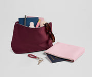 Maroon pouch with pink pouch and travel items on a light gray background