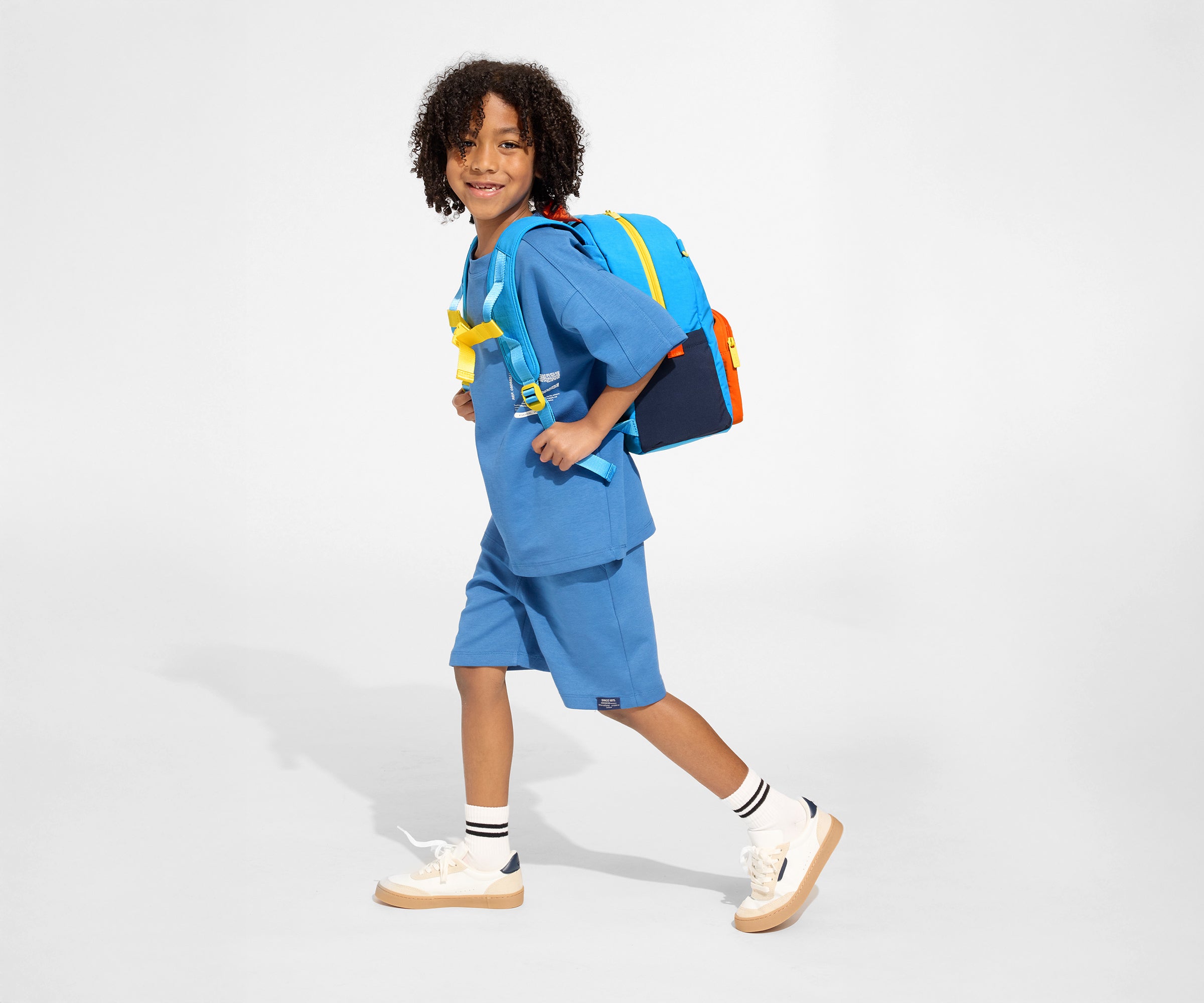 A child model wearing the Kids Backpack in Splash Blue with the chest strap in use