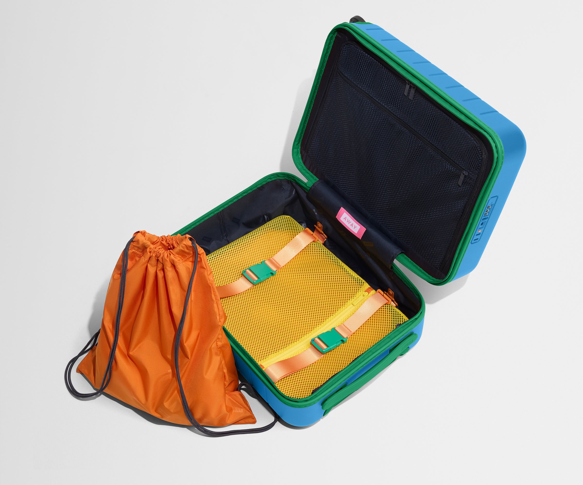 The Kids Carry-On suitcase in Splash Blue shown open and empty on its side to show capacity, and an orange laundry bag can double as a backpack for smaller travelers.