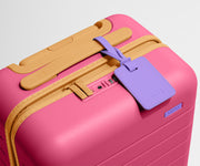 The Kids Carry-On suitcase in Cotton Candy Pink shown shown from above highlighting TSA-approved combination lock and colorful silicone luggage tag