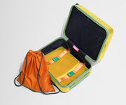 The Kids Carry-On suitcase in Sunshine Yellow shown open and empty on its side to show capacity, and an orange laundry bag can double as a backpack for smaller travelers.