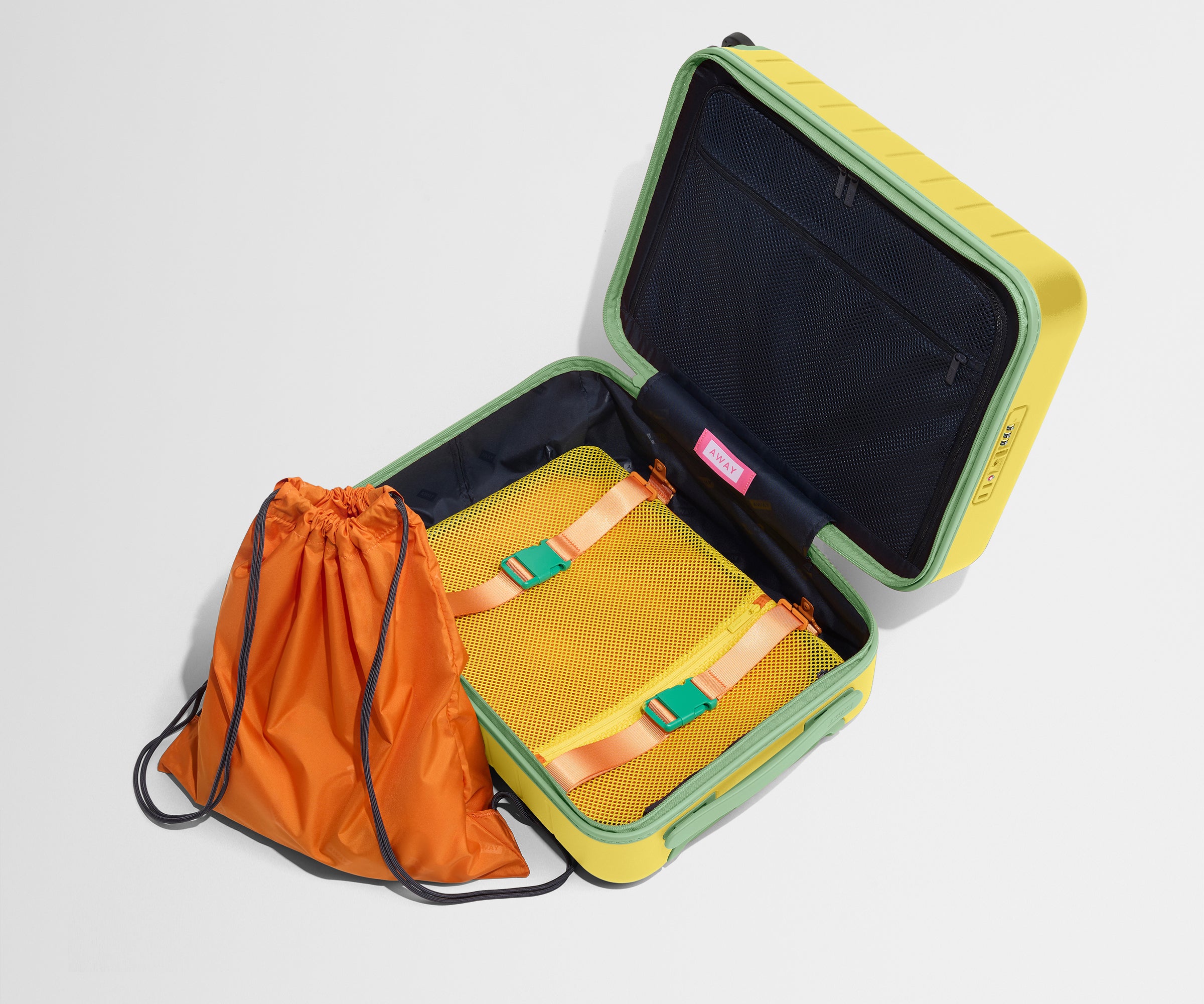 The Kids Carry-On suitcase in Sunshine Yellow shown open and empty on its side to show capacity, and an orange laundry bag can double as a backpack for smaller travelers.