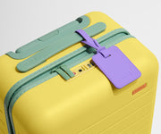 The Kids Carry-On suitcase in Sunshine Yellow shown shown from above highlighting TSA-approved combination lock and colorful silicone luggage tag